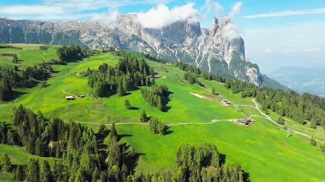 Dolomite cliffs beyond Alpe di Siusi pastures and farm tracks, aerial view. High-altitude plateau scenery in South Tyrol
