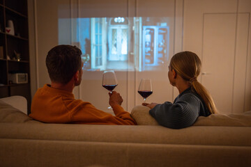 Pair relaxing together during nighttime date sharing drinks and watching film via projector in dim...