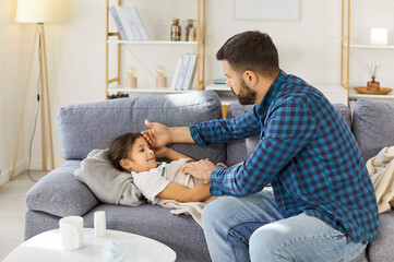 Child fever virus, father checks temperature. At home, a sick girl rests as a caring parent checks illness, offers medicine and comforts her. Healthcare and parental care during childhood illness.