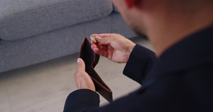 Man drops coin into leather wallet. Close-up male hand manages money at home, showing finance discipline, budget planning, late payment, and rebuilding savings. Bankrupt, no money, financial crisis