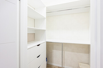 A bright, white walk-in closet features shelving, drawers, and hanging space. The design is modern and minimalist, emphasizing clean lines and organized storage