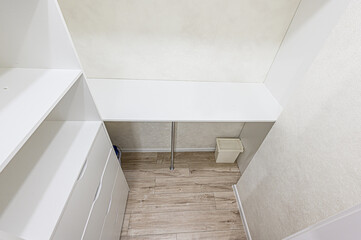Fototapeta premium A closet space with white shelving, drawers, a desk area, and a trash bin on a wood-look floor