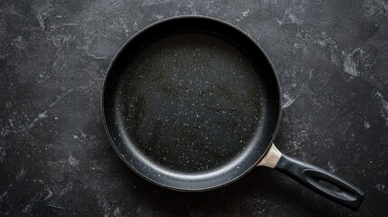 A black frying pan with a handle on a dark, textured surface.