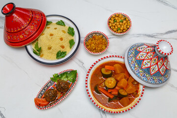 Couscous aux boulettes – plat maghrébin traditionnel avec semoule, légumes et boulettes de viande, servi dans de la vaisselle traditionnelle sur table en bois blanche. Cuisine marocaine.