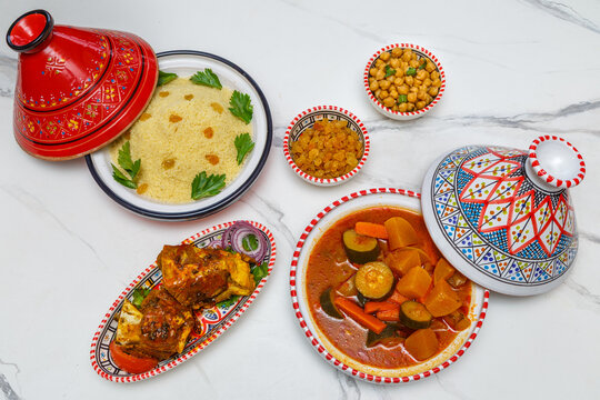 Couscous à l’agneau – plat maghrébin traditionnel avec semoule, légumes et morceaux d’agneau, servi dans de la vaisselle traditionnelle sur table en bois blanche. Cuisine maghrébine