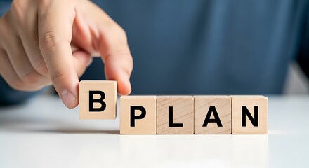 Hand arranging wooden blocks with letters spelling out the word b plan, representing a business plan or strategy