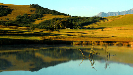 Beautiful landscape photo of a dam on an early misty morning, trees, mountains in the background, and reflections in the blue water.