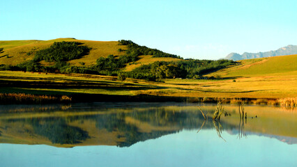 Beautiful landscape photo of a dam with a boat in the foreground, trees, mountains in the background, and reflecting in the dam. 