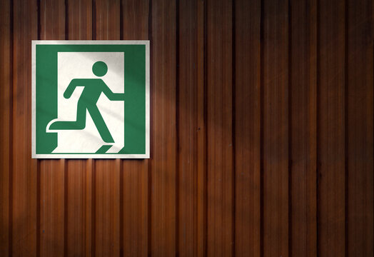 Fire exit sign on the right on a brown metal panel. Background space for copy text. Yellow light effect.	
