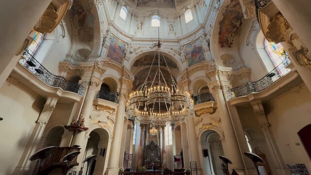 Exterior and interior views of the monumental St. Nicholas Church in Prague. Baroque dome frescoes, massive chandeliers, and intricate gilded stucco contrast with the passing city tram.