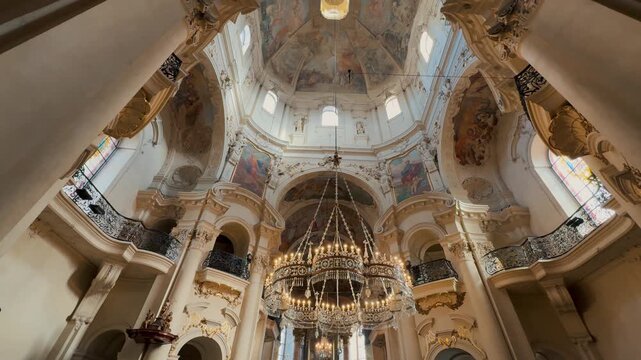 Exterior and interior views of the monumental St. Nicholas Church in Prague. Baroque dome frescoes, massive chandeliers, and intricate gilded stucco contrast with the passing city tram.