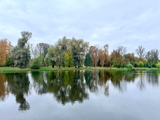 autumn trees reflection on the lake surface in the park, gloomy grey sky, melancholic atmosphere