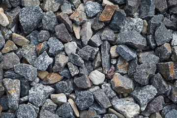 Full-frame close-up of dark grey, white, and brown crushed granite or gravel, providing a rough, natural, and textured background suitable for construction, landscaping, and geology themes.