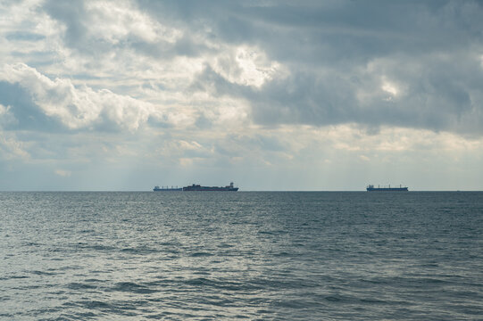 Several cargo ships floating on a tranquil sea with a dramatic cloudy sky above.	
