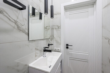 Sleek bathroom featuring white marble tiles, modern sink, black fixtures, and a white door. Minimalist design