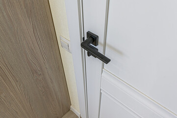 close-up of a white door with a modern, black, square door handle. Adjacent walls show light wood paneling