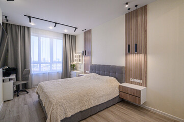A modern bedroom with a cozy bed, wooden panel accents, and sleek lighting. Natural light streams through the window