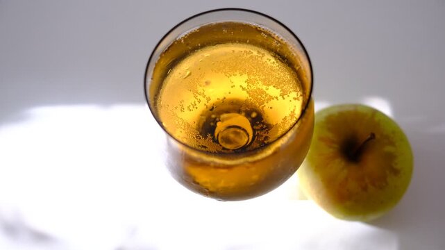 Glass of brut apple cider from Normandy. White table with casting shadows and sunlight. Ripe yellow fruits on the table. Atmospheric mood.	