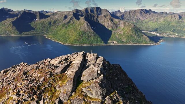 Man on top of mountain Segla, Senja island. Hiker reach the summit and admire breathtaking views of mountains and water in Norway. Aerial drone shot with orbit motion 