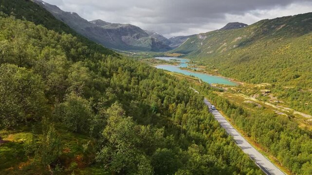 Stunning landscapes of Jotunheimen National Park with turquoise lakes and lush green hills, Norway. Traveling by camper. Car moves along road in Jotunheim National Park, aerial view