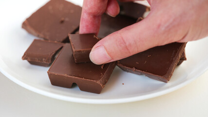 A man taking a piece of broken milk chocolate from a plate. Close up.