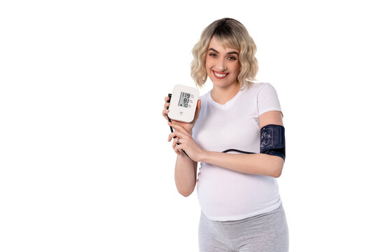 Woman measures her blood pressure at home with a digital device during pregnancy in a well-lit room