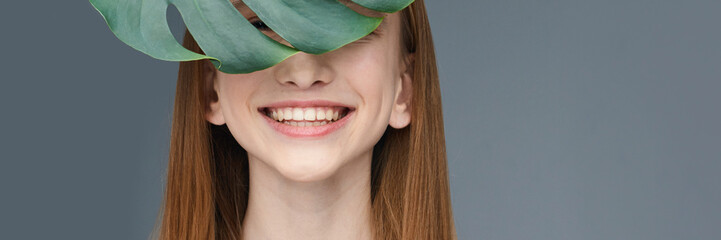 Smiling young caucasian female with red hair and leaf in portrait against gray background.