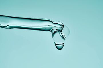 A drop of serum drips from a pipette on a delicate green background.