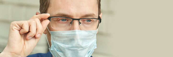 Caucasian male adult adjusting glasses while wearing protective face mask in urban setting.