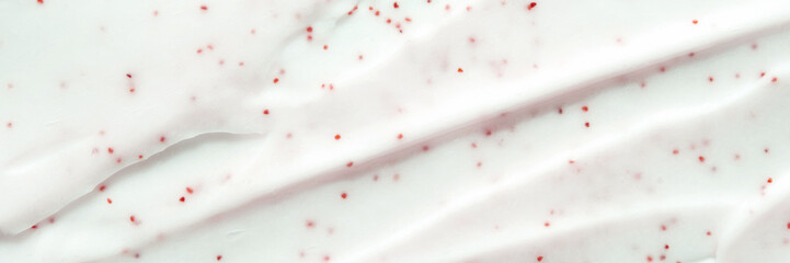 Close-up of white cream with red particles creating texture and patterns on smooth surface.