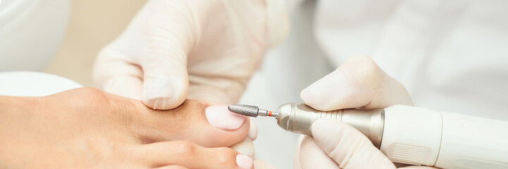 Close-up of professional pedicure: foot care with electric nail file by caucasian mature female in...