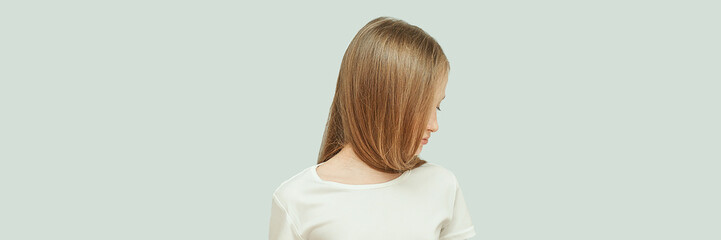 Fototapeta premium Caucasian female child with long brown hair looking sideways in white t-shirt on light gray background.