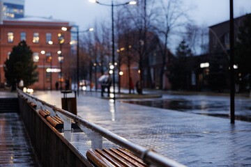 A serene evening walk in a quiet city street, illuminated by warm lamplight amidst the gentle rain.