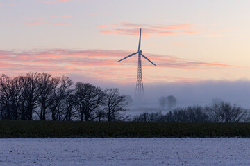 Windkraft im Kalletal an einem kalten verschneiten und klaren Winterabend in einer wundersch&ouml;nen Schneelandschaft bei einem pastellfarbenen Sonnenuntergang Windrad zwischen B&auml;umen und Feldern 