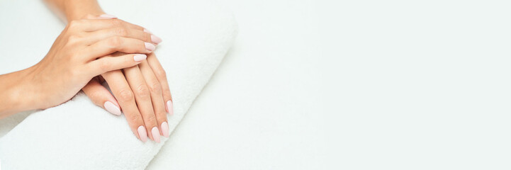 Close-up of female hands with light pink manicure resting on white towel, showing elegance and care.