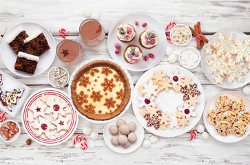 Christmas holiday cookies and desserts table scene. Top down view on a white wood background. Eggnog pie, a variety of cookies, fruit cake, cupcakes and chocolate eggnog.