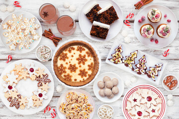 Christmas holiday cookies and desserts table scene. Overhead view on a white wood background. Eggnog pie, a variety of cookies, fruit cake, cupcakes and chocolate eggnog.
