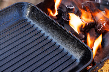 Heat radiates as a cast iron grill pan rests on fiery coals, ready for a summer barbeque with friends and family.