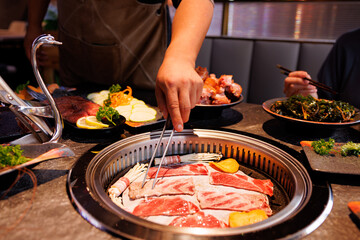 Friends gather around a grill, savoring fresh cuts of meat and cheerful conversations in a cozy restaurant setting.
