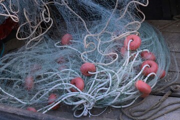 Close-up of tangled fishing net with red floats and ropes on a wooden deck, traditional marine equipment for catching fish at sea.