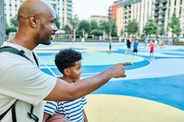 African american father and boy smiling, standing together playing basketball on a colorful...