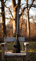 lone black broomstick sits atop weathered wooden chair warm golden autumnal backdrop bare