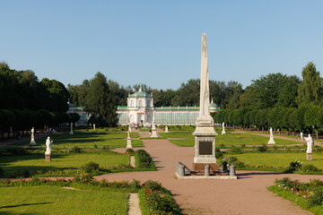 Visitors stroll through a lush garden featuring statues and an impressive obelisk surrounded by greenery and flowers.