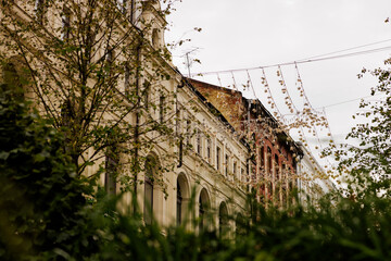Obraz premium Elegant buildings showcase detailed architecture with festive decorations hanging above, surrounded by foliage.