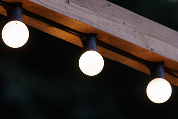Softly glowing lights hang from a wooden beam, casting warm light in a peaceful outdoor space at...