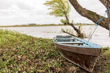 Abandoned boat on riverbank under cloudy sky, evoking solitude.