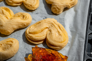 Unbaked sweet buns placed on a baking tray next to a sheet of brown caramel. Concept of high-sugar and high-carbohydrate homemade pastries and desserts.