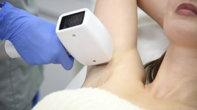 laser epilation, hair removal procedure, young beautiful caucasian smiling brunette woman lying on couch in beauty salon, armpits epilation, spa and cosmetology concept