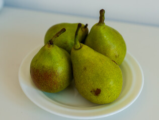 Close-up of ripe green pears resting on a white dish. The simple still life emphasizes natural color, organic freshness, and clean minimal composition perfect for food themes.
