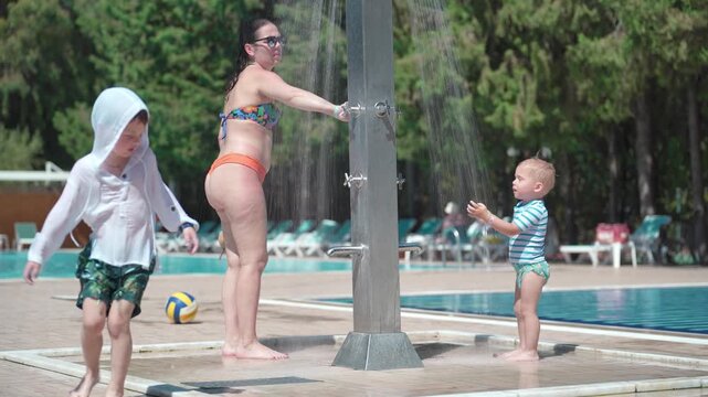 Two young children and their mother are washing in the shower next to the swimming pool.